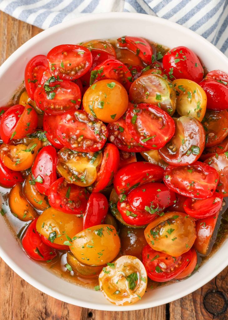 the balsamic marinated tomatoes in a white bowl with a blue and white striped napkin visible in the background