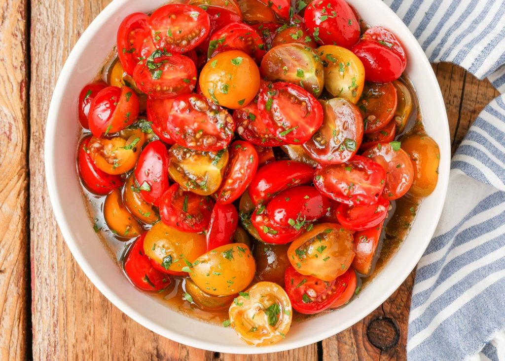 a horizontally aligned photo of a white bowl filled with marinated tomatoes