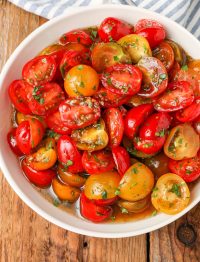 a top down photo of a bowl of marinated tomatoes with a blue and white striped tea towel visible in the background
