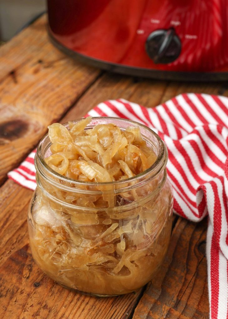 An image of a small jar containing caramelized onions with an image of a red slow cooker in the background