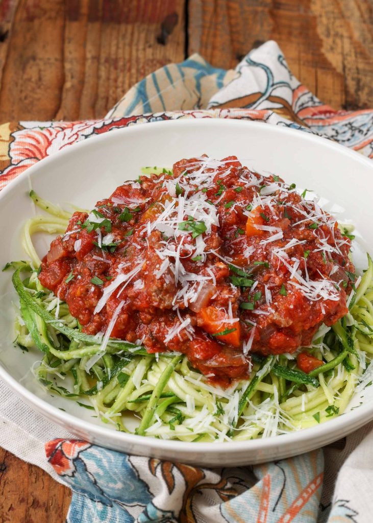 zucchini noodles with marinara sauce in white bowl on wooden table