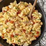 potato salad with bacon and corn in black bowl with wooden spoon
