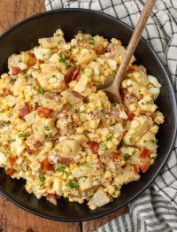 potato salad with bacon and corn in black bowl with wooden spoon