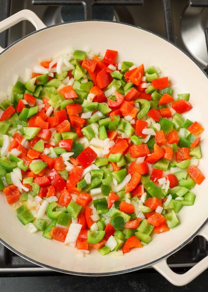 Raw bell peppers and onions in a white cooking pot on a black stovetop