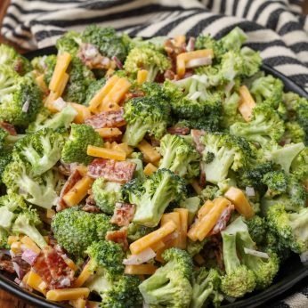 Overhead vertical shot of broccoli cheese bacon salad in black bowl with striped black and white towel