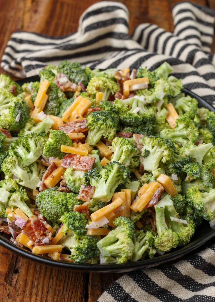Overhead vertical shot of broccoli cheese bacon salad in black bowl with striped black and white towel
