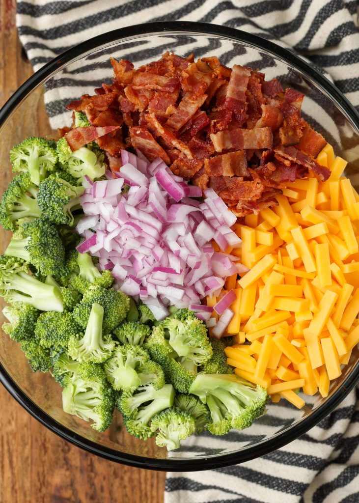 Broccoli salad ingredients in clear bowl with striped towel