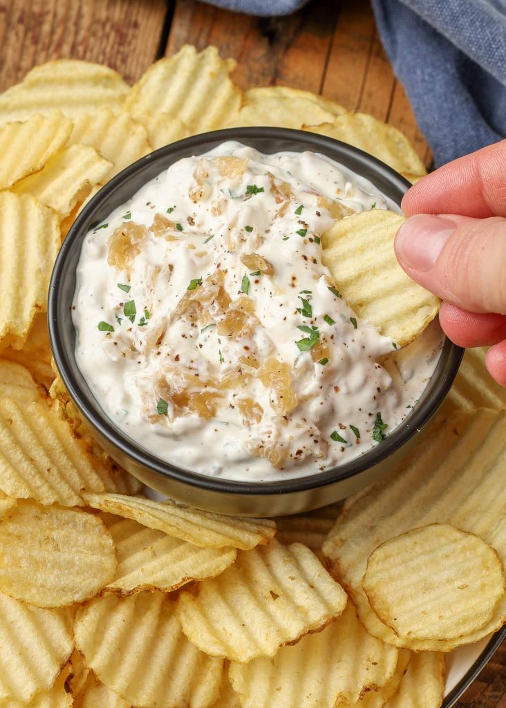 hand holding a chip dipping into onion dip