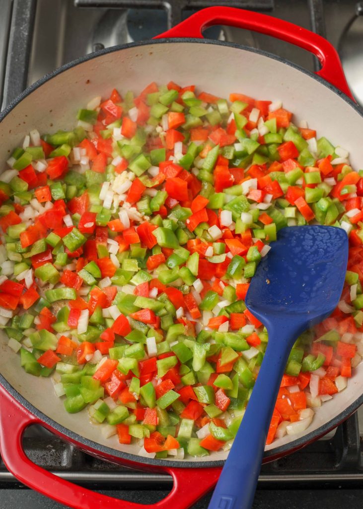 Overhead shot of bell peppers and onions in a red and white pot with a blue spatula