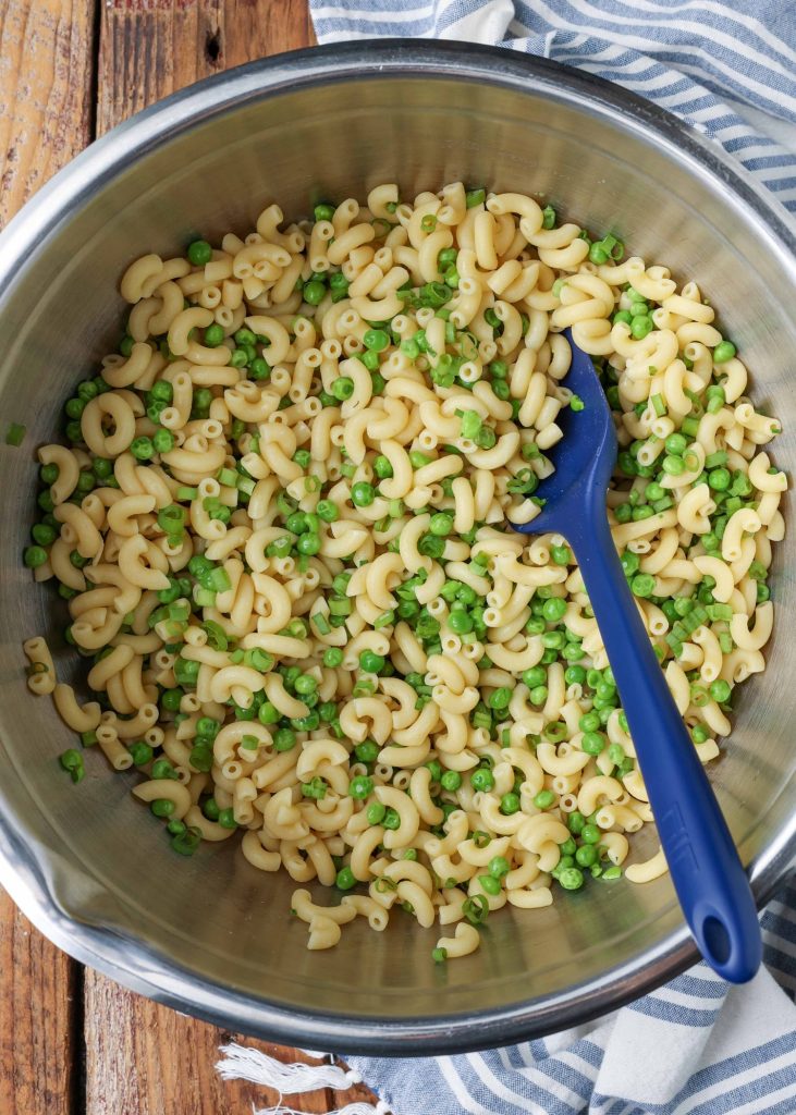 Pasta and peas in a stainless steel bowl with a blue rubber spatula