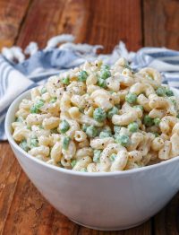 Creamy pea pasta salad with bacon and cheese in a white bowl with a striped blue and white towel