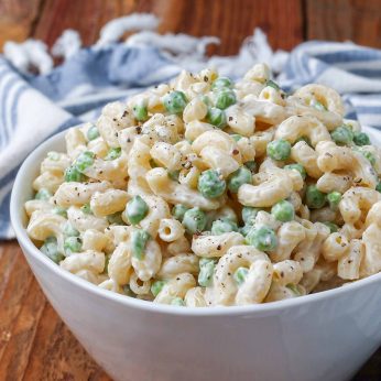 Creamy pea pasta salad with bacon and cheese in a white bowl with a striped blue and white towel