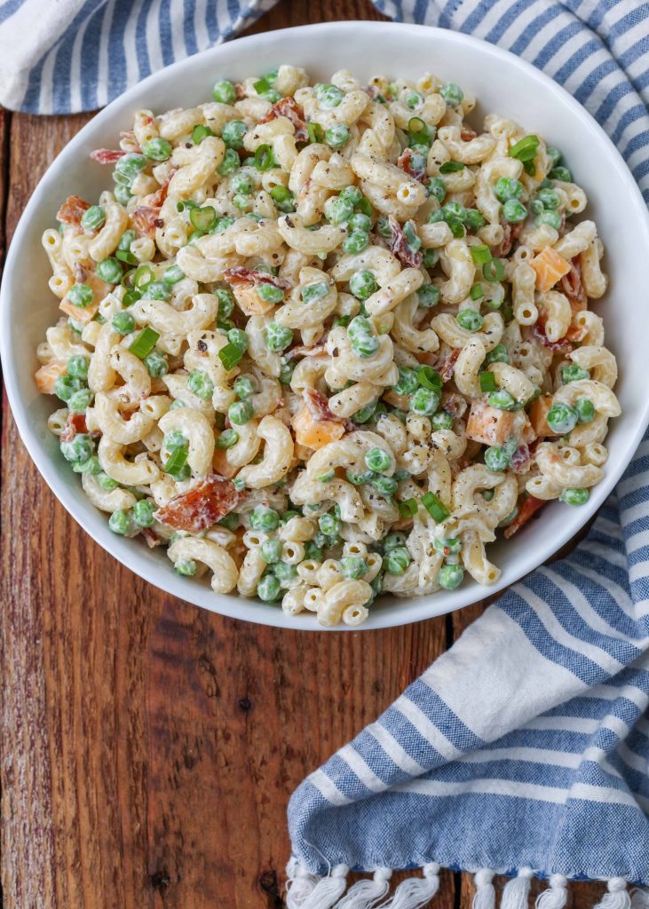 Overhead shot of creamy  pea pasta salad with bacon and cheese in a white bowl with a striped blue and white towel