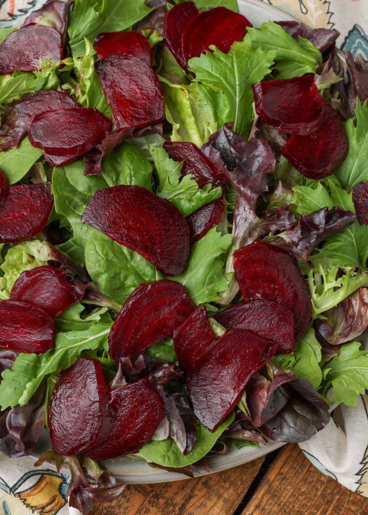 sliced roasted beets have been laid over the greens for the salad in this top down shot