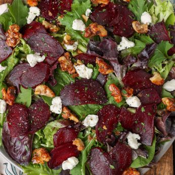 a roasted beet salad has bits of goat cheese and candied walnuts atop it, ready to serve