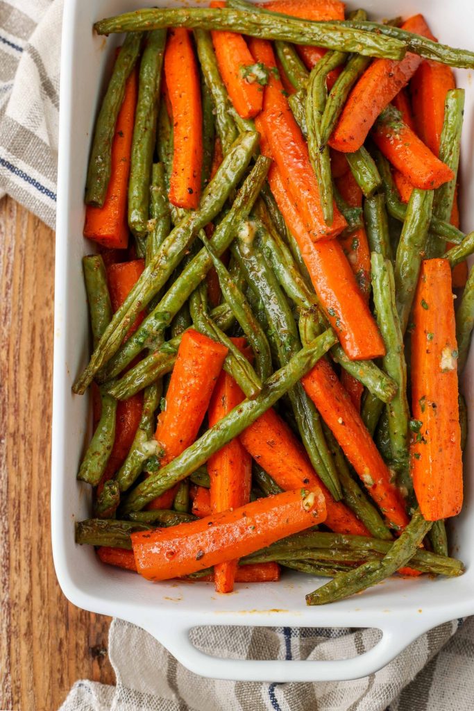 Overhead vertical shot of roasted carrots and green beans in a long white tray