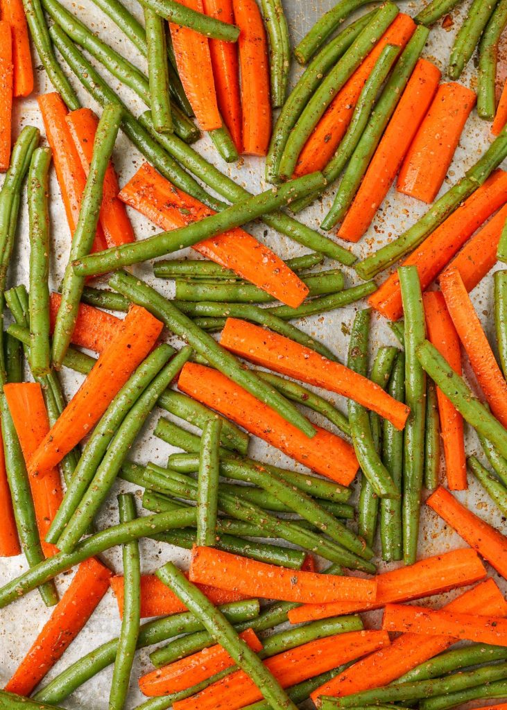 Raw carrots and green beans on a baking sheet