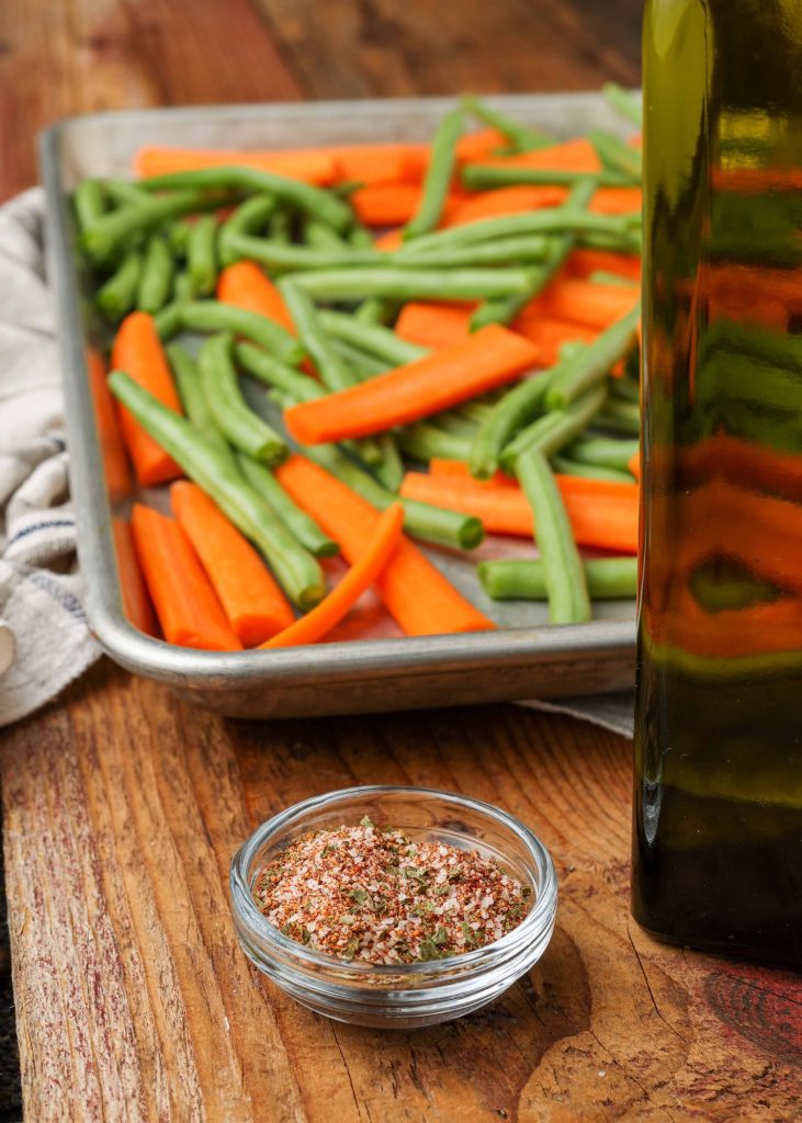 Raw carrots and green beans on a tray next to a small glass bowl of spices