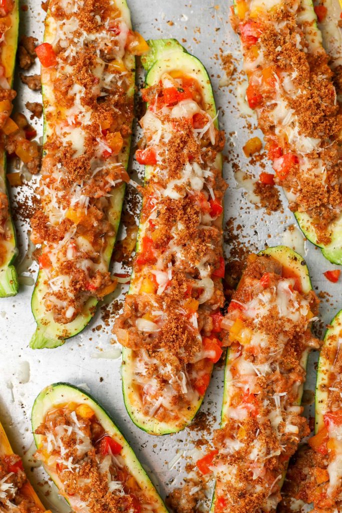 Overhead shot of zucchini stuffed with sausage, bell peppers, and cheese in baking sheet