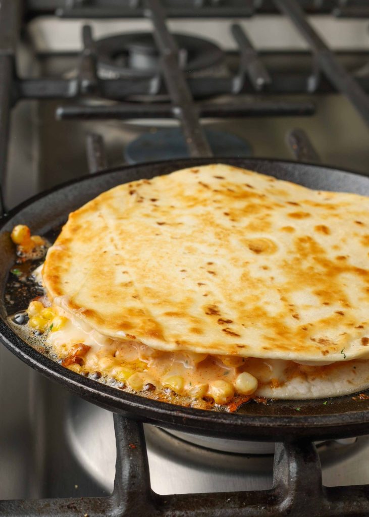 Corn quesadilla cooking in a skillet; the top tortilla has already been browned