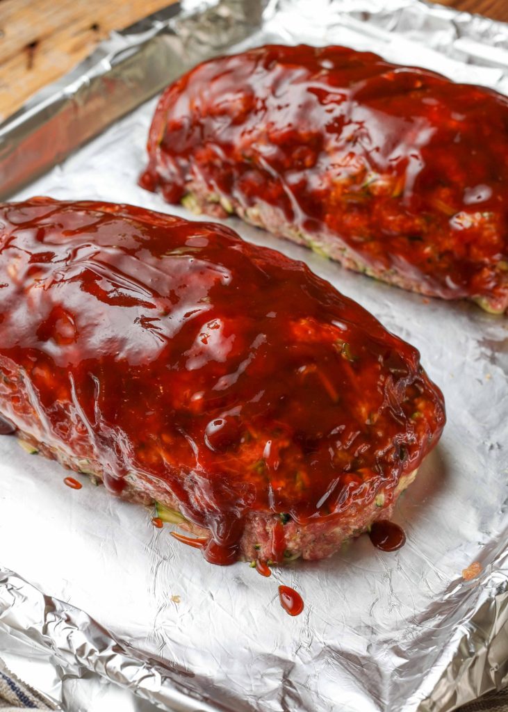 Overhead diagonal shot of two prepped meatloaves covered in homemade BBQ glaze, ready to go into the oven, served on a long white rectangular platter