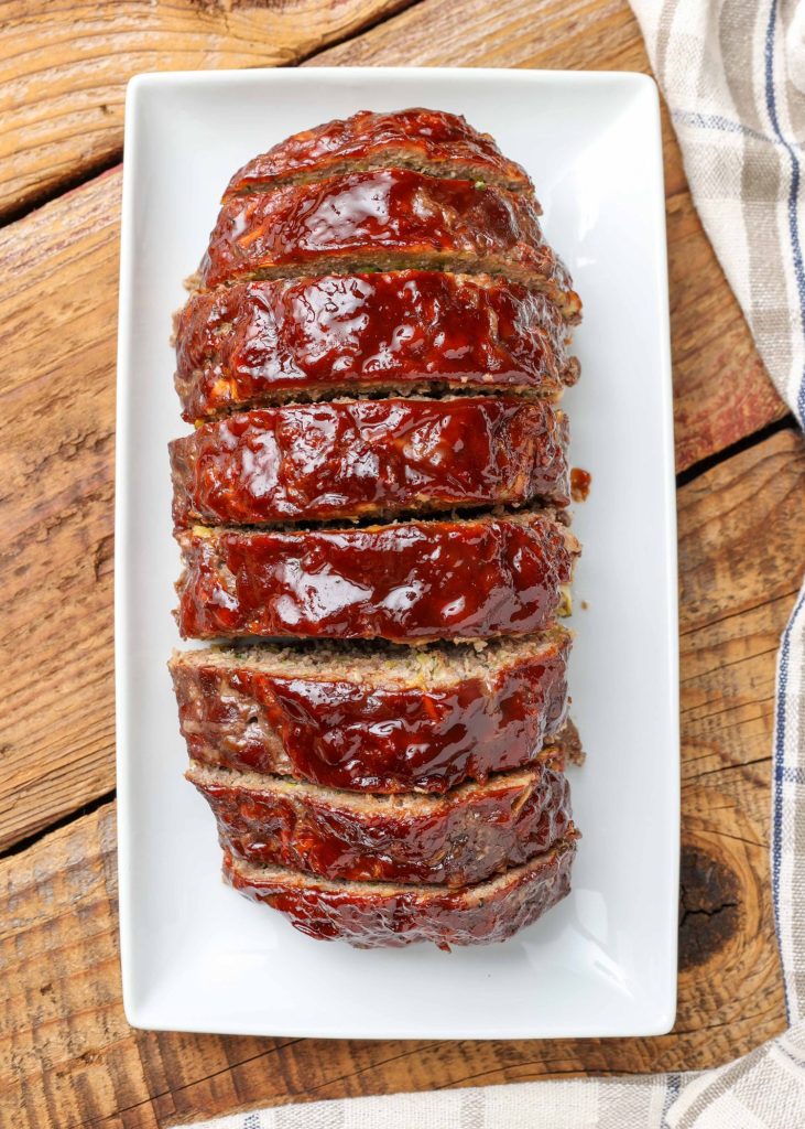 Overhead vertical shot of large sliced meatloaf topped with BBQ sauce, served on a long white rectangular tray