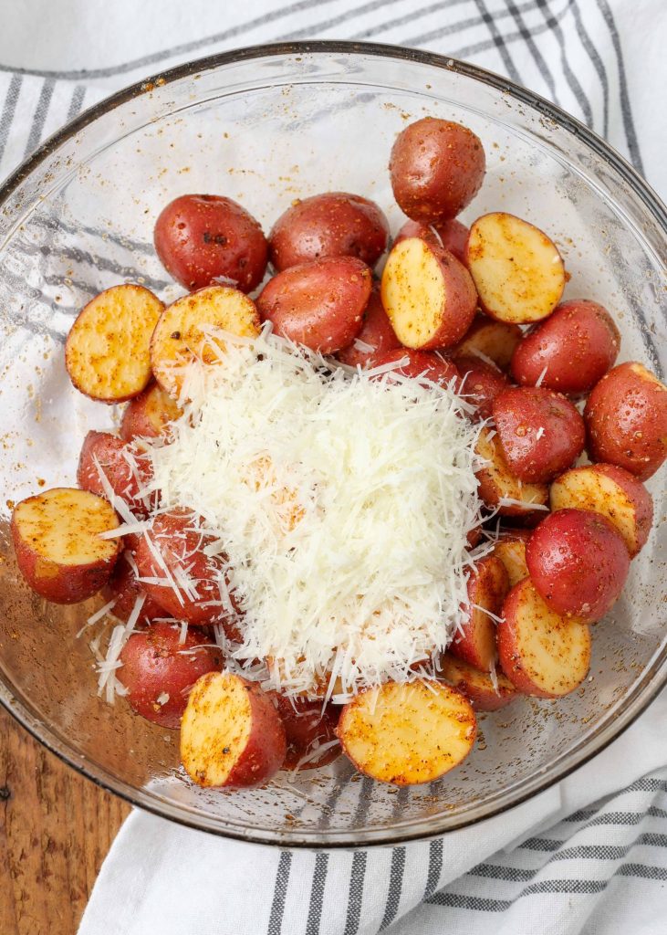 raw potatoes coated with spices and cheese in clear bowl