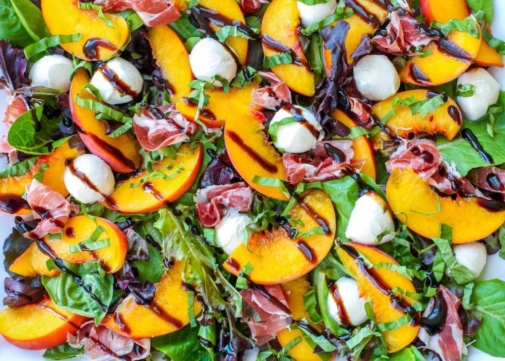 close up of peaches, mozarella, and baby greens