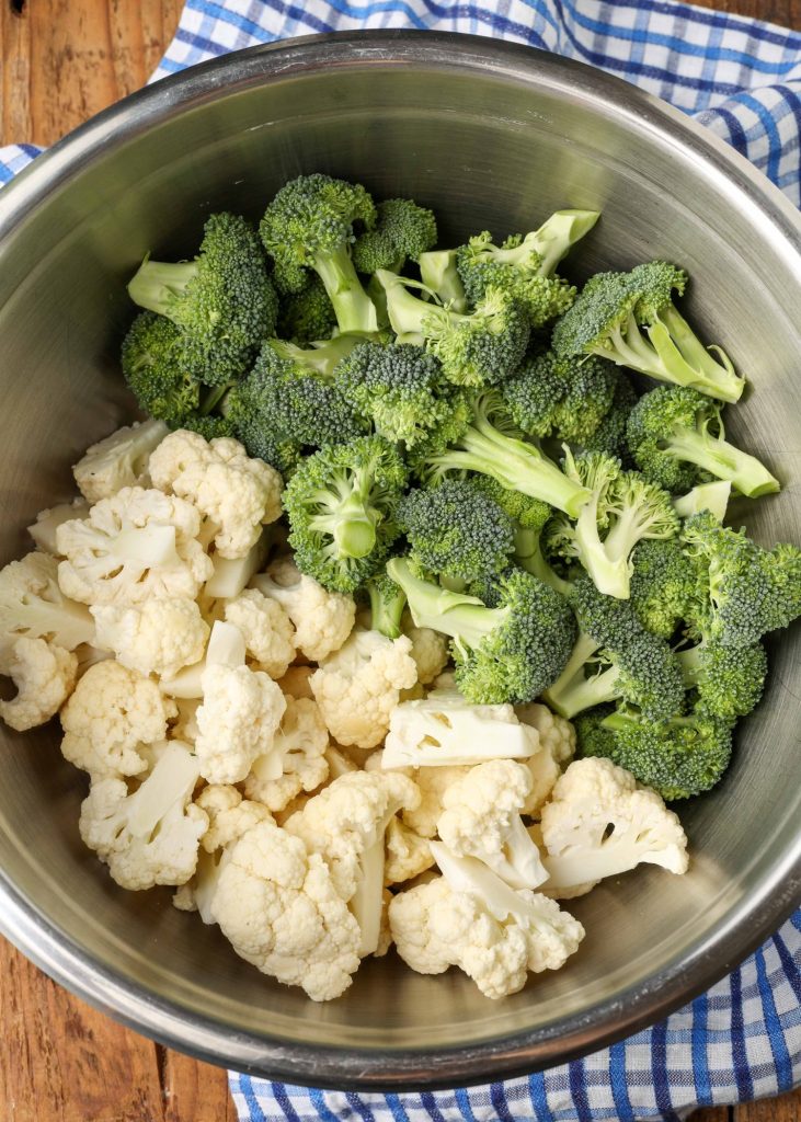 broccoli and cauliflower in metal mixing bowl over blue gingham napkin
