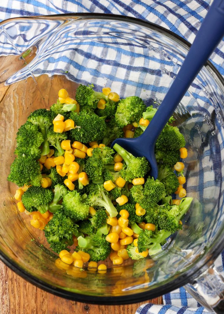 Broccoli and corn have been placed into a clear glass mixing bowl on a wooden tabletop