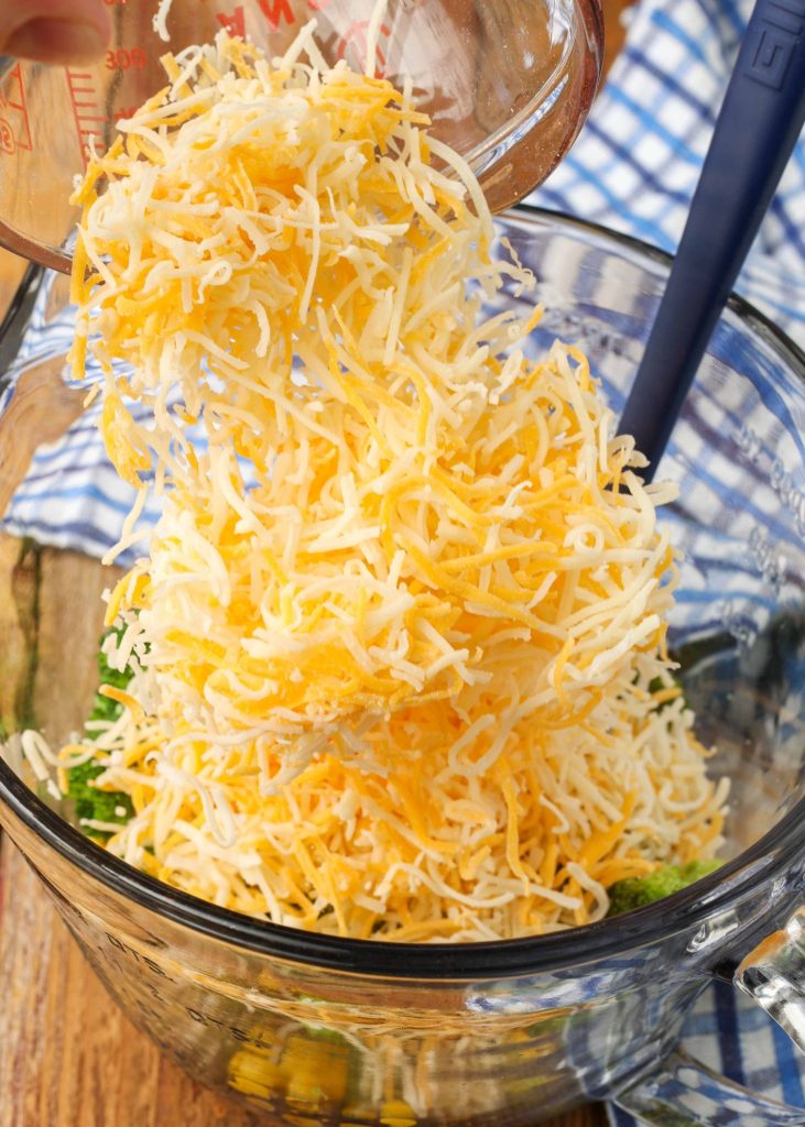 Adding the shredded cheese to the mixing bowl with the vegetables from the microwave