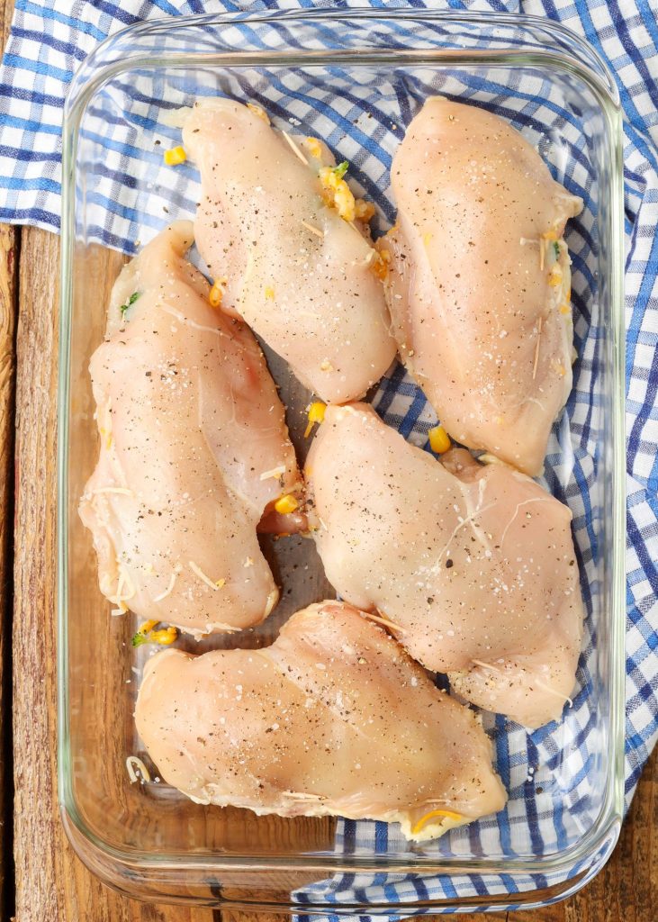 Chicken breasts have been stuffed with cheddar and broccoli and placed into a glass baking dish.