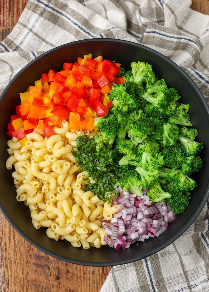 Pasta, chopped bell peppers, broccoli florets, and diced onions, portioned in a large black bowl
