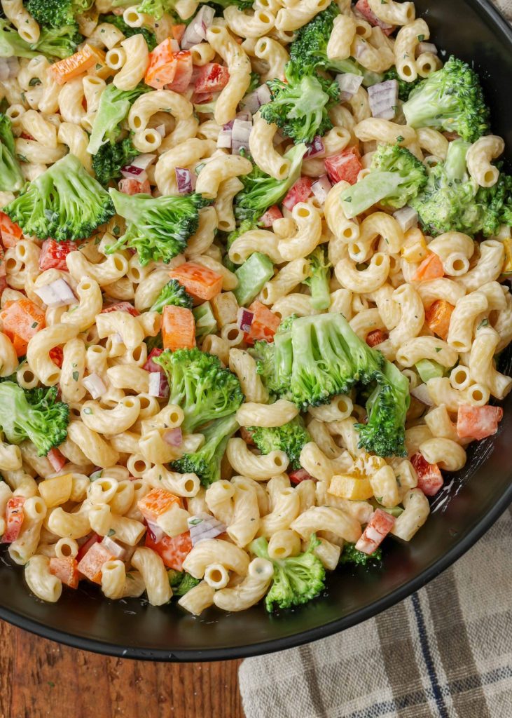 Overhead shot of broccoli pasta salad, served in a white bowl with a checkered white and gray towel