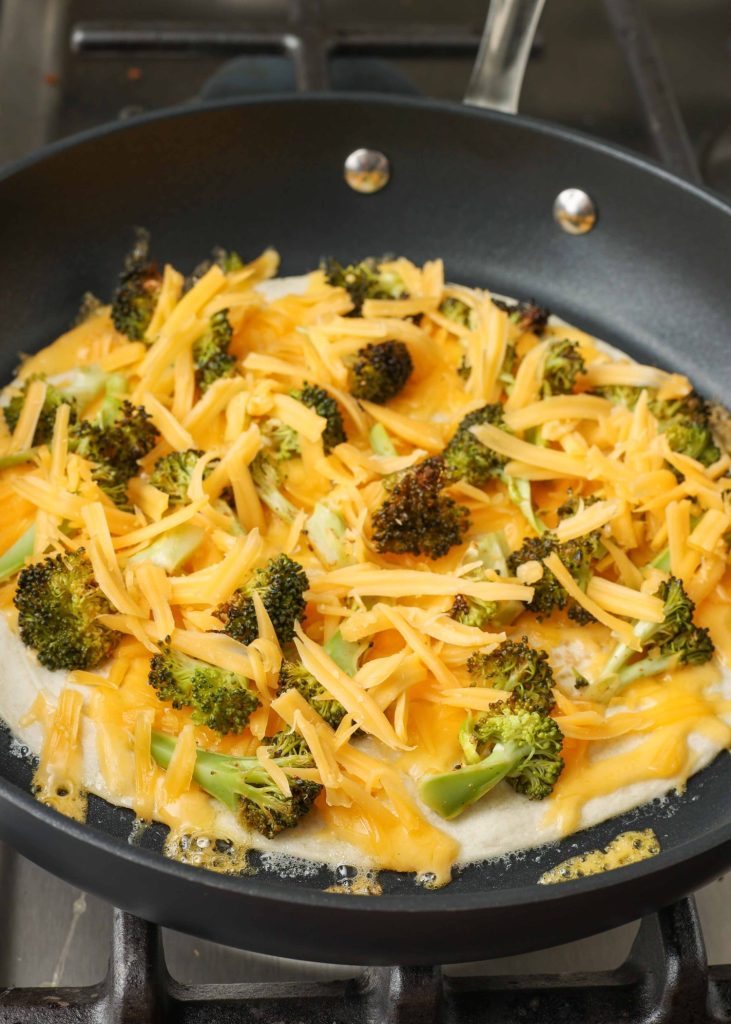 Overhead shot of open-face cheesy broccoli quesadilla cooking in a nonstick skillet