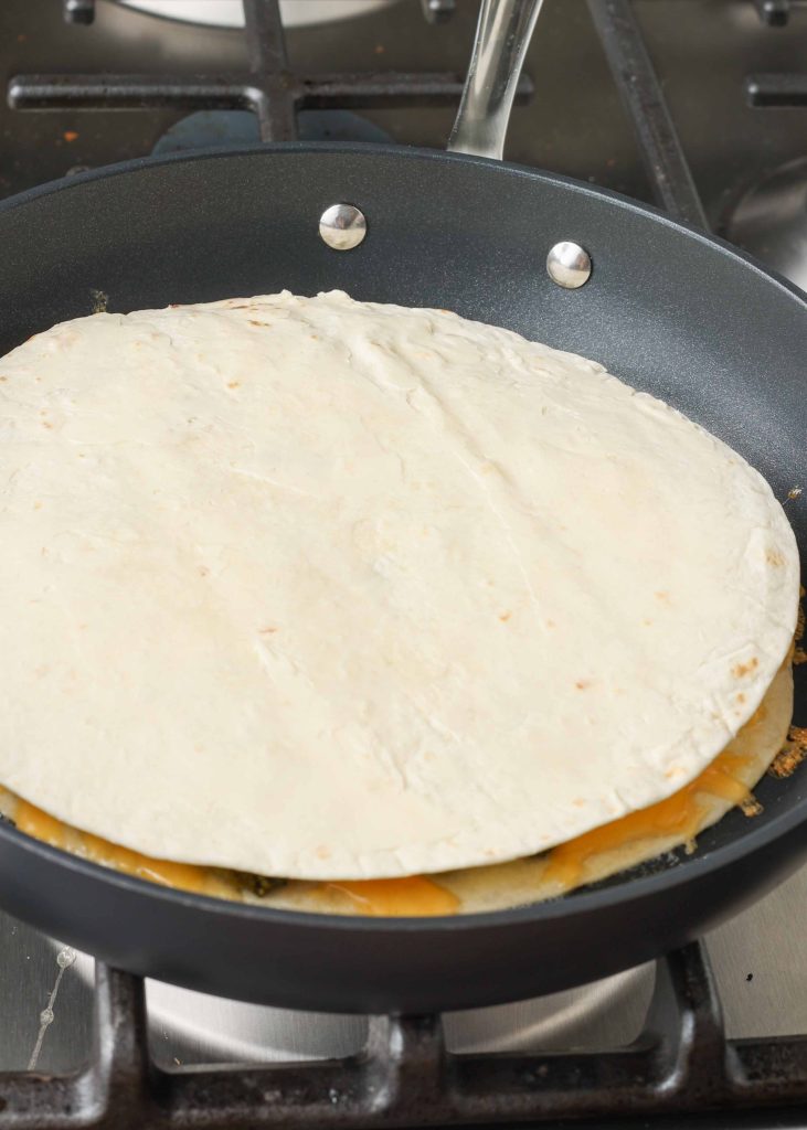 Overhead shot of a newly topped cheesy broccoli quesadilla beginning to cook along the skillet's surface