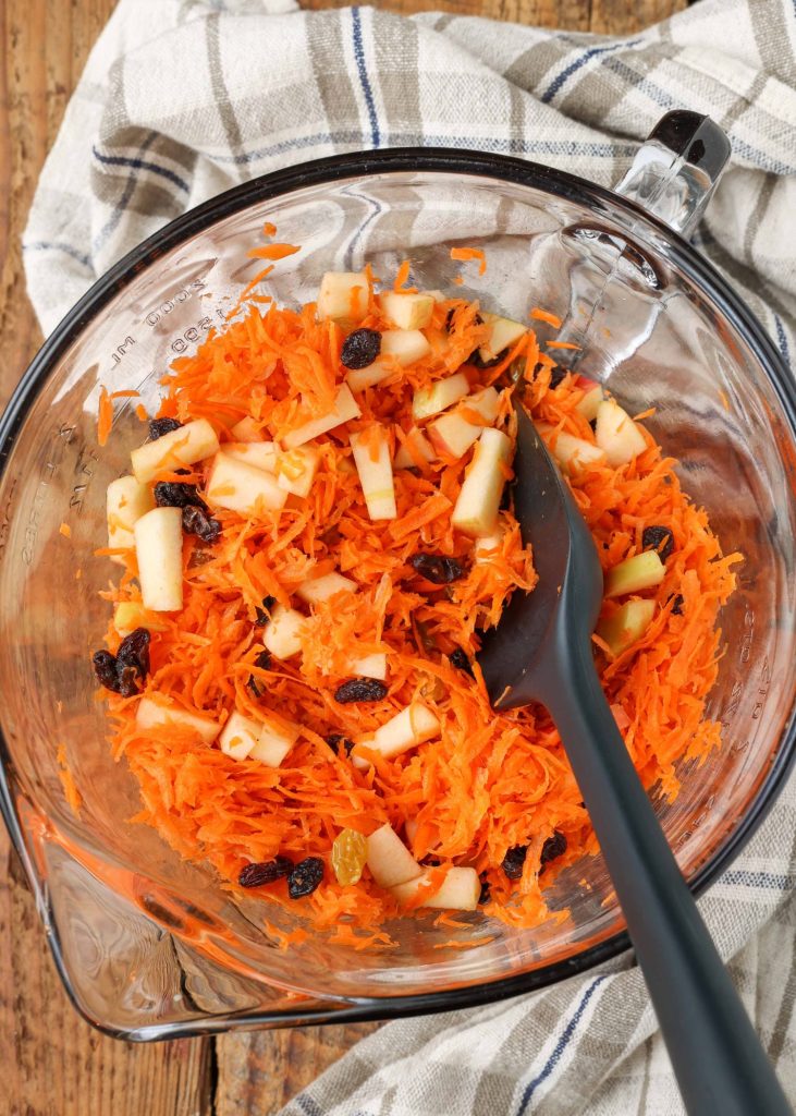 Overhead shot of tossed carrots, apples, and mixed raisins, served in a glass bowl