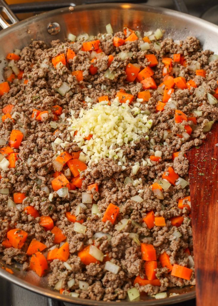 Adding the seasonings to the ground beef mixture in a skillet on the stove.