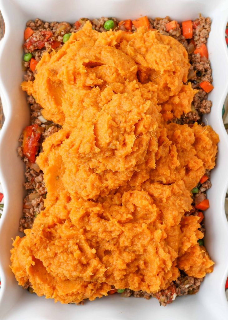 Placing the mashed sweet potatoes on top of the ground beef filling.