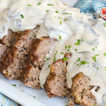A white gravy laden with mushrooms has been poured over these slices of meatloaf.