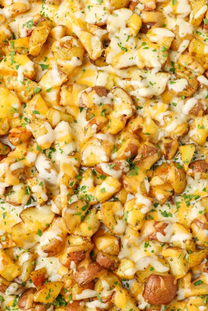 A vertically aligned, close up shot of cheesy roasted potatoes, sprinkled with fresh herbs.