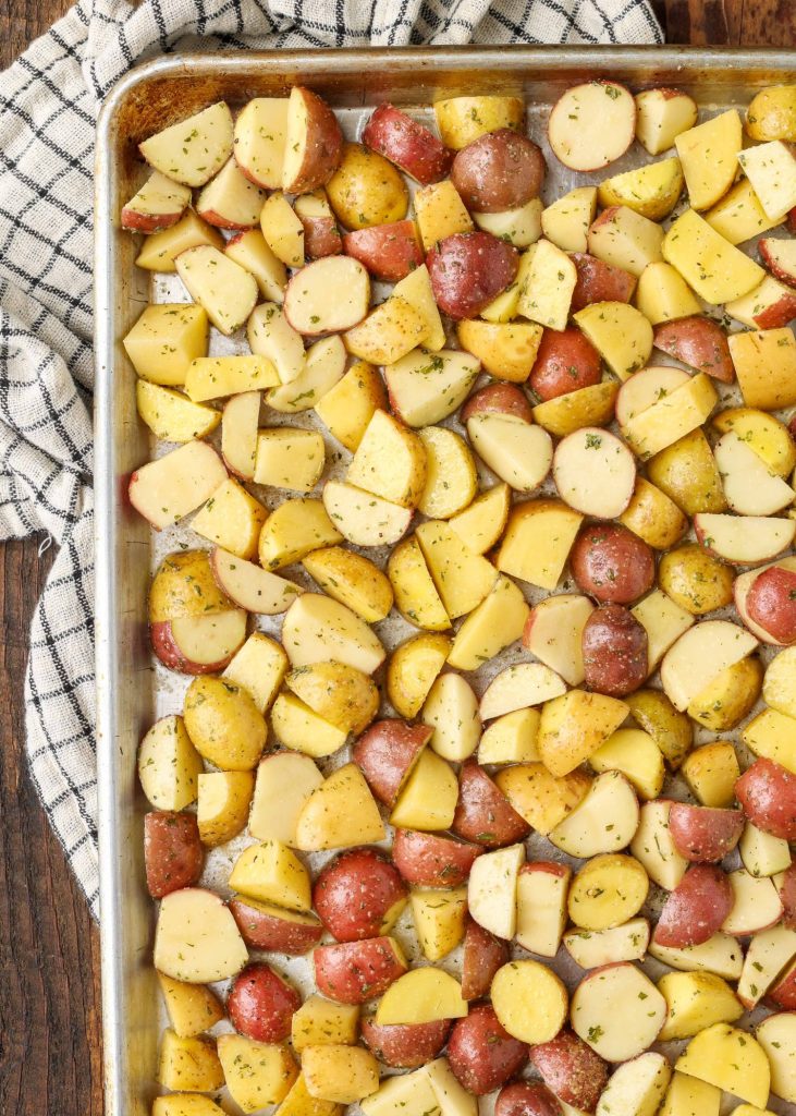 A sheet pan is loaded with sliced potatoes that are seasoned well.