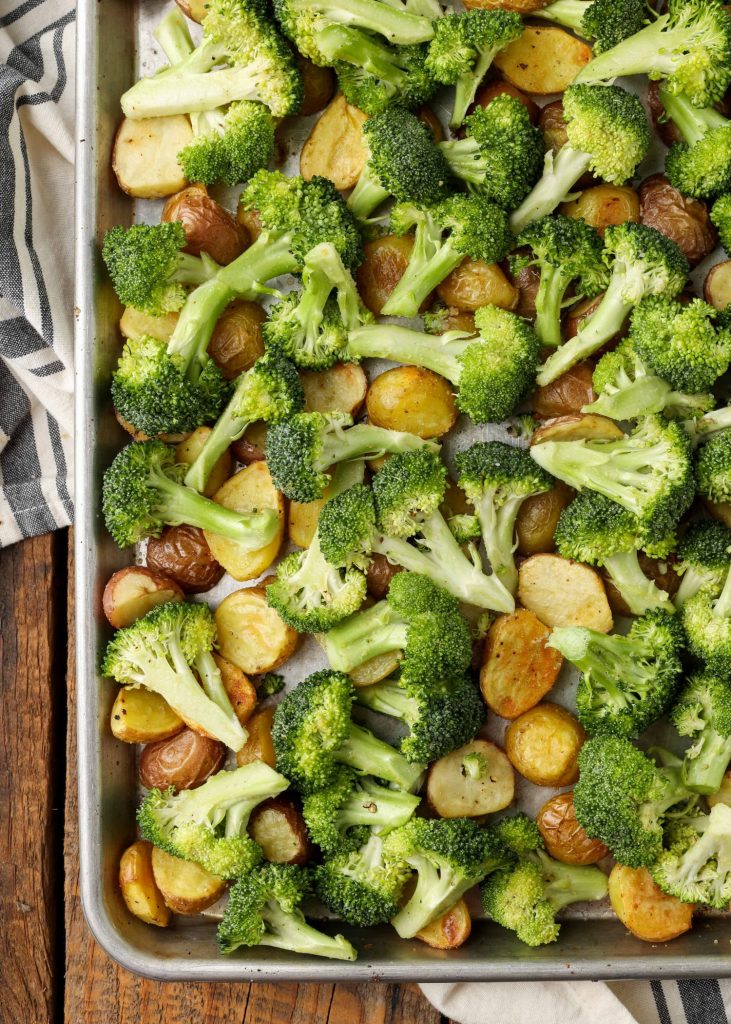 A sheet pan loaded with broccoli and potatoes, ready to be placed in the oven.