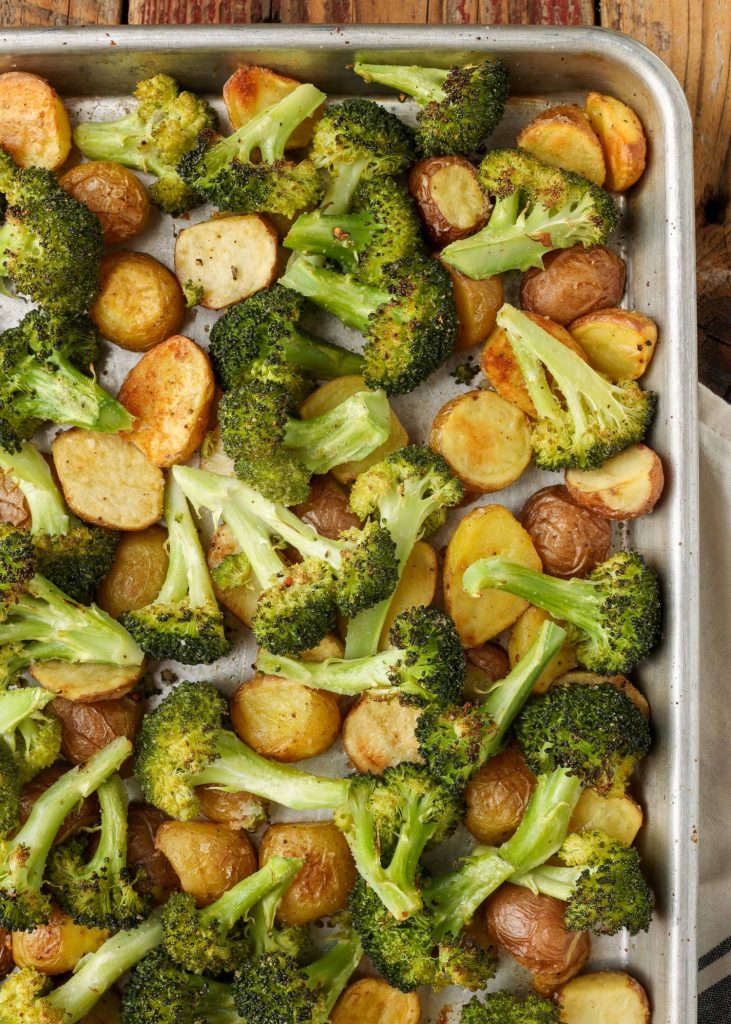 A vertically aligned, top down shot of one corner of a metal sheet pan heaped with broccoli and potatoes, fresh from the oven.