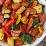 a top down photo of a bowl of sausage zucchini skillet on a wooden tabletop.