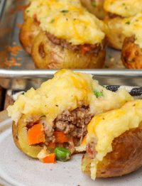 One of the baked potatoes with meat and vegetable filling has been cut in half, to reveal its inner structure.