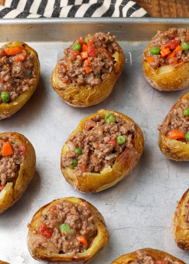 The baked potatoes are on a metal pan, filled with the meat and vegetable filling.