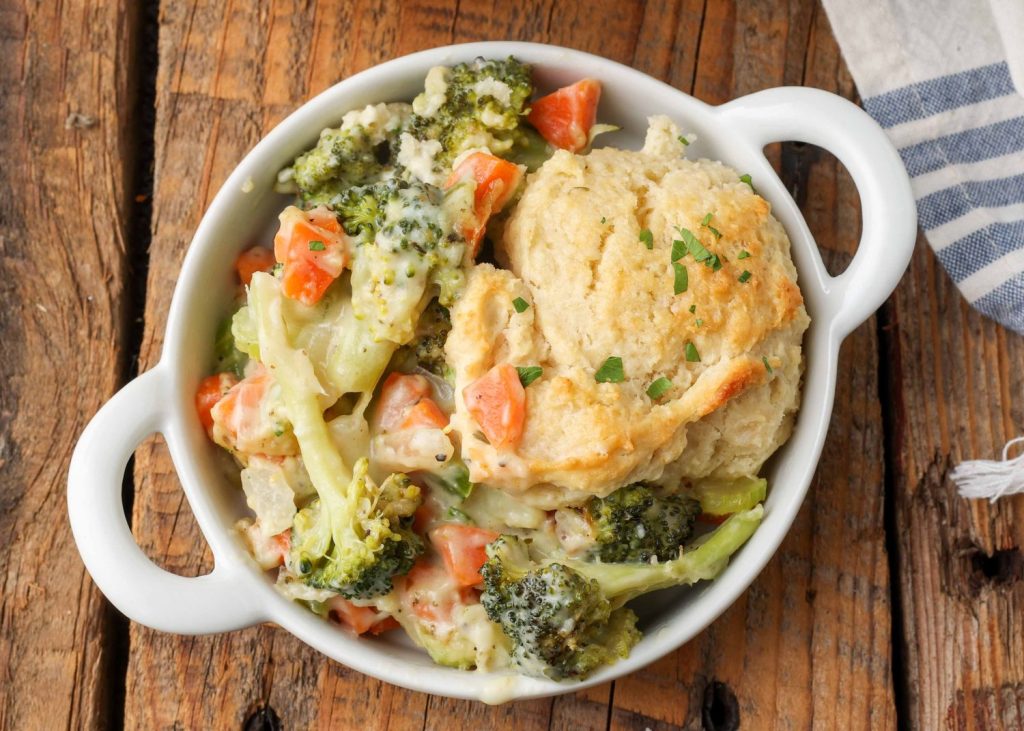 white dish filled with vegetables in a cream sauce topped with a golden biscuit