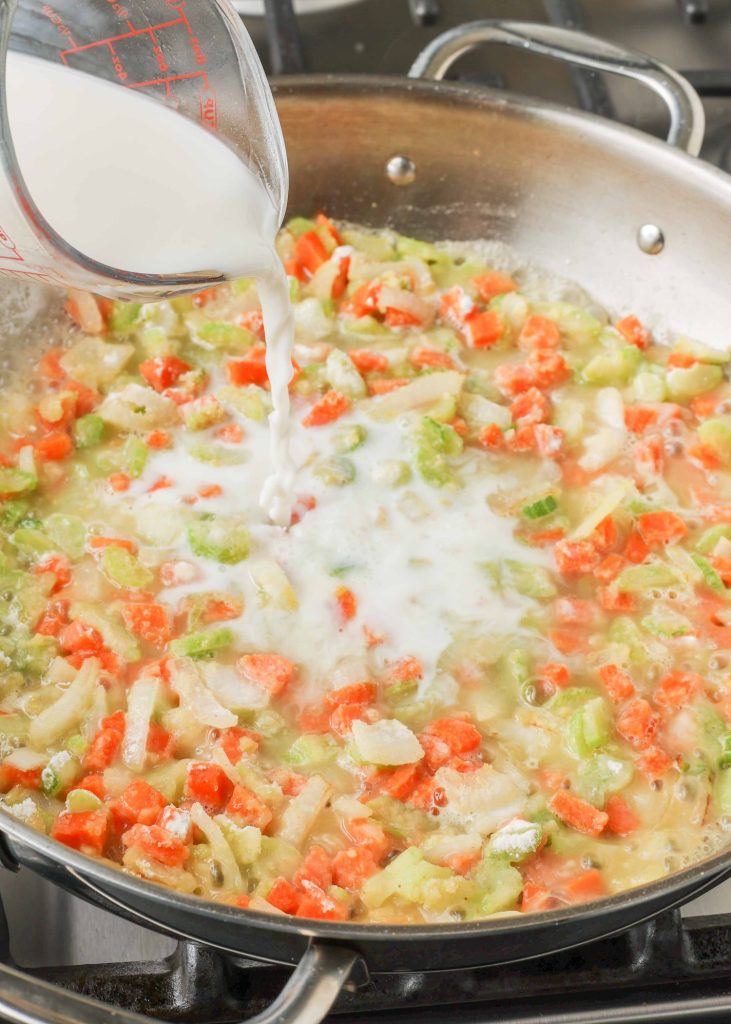 cream sauce being poured into skillet of vegetables for pot pie