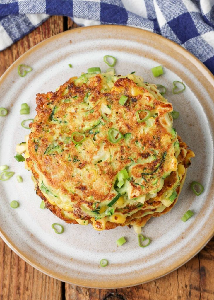white plate holding zucchini fritters with green onions on top next to blue napkin
